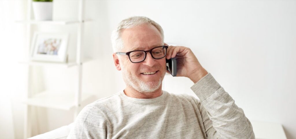 man in his living room, holding a phone up to his ear and talking with a counsellor through the phone, phone counselling
