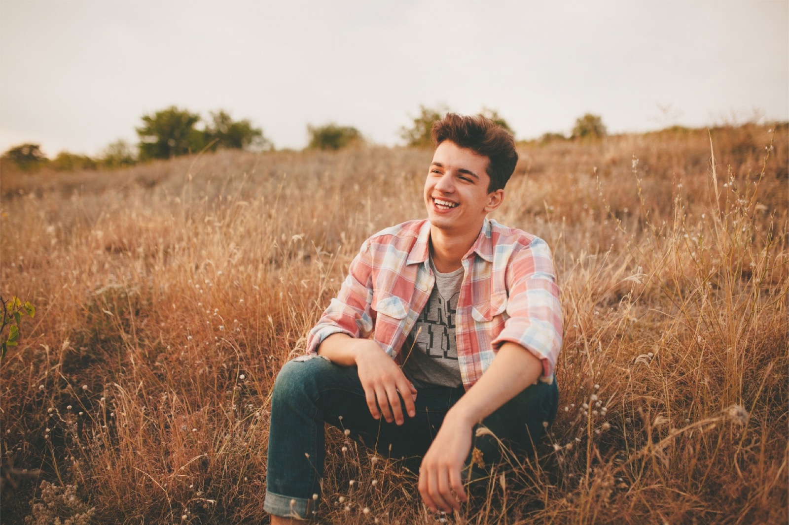 young man sitting in a field, smiling, happy with life.